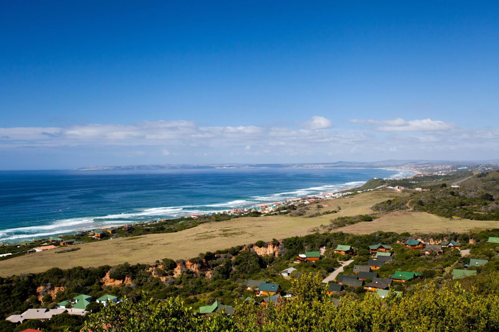Blick von einem Hang über Ferienhäuser auf die Bucht von Mossel Bay und einen langen Strand Richtung Osten