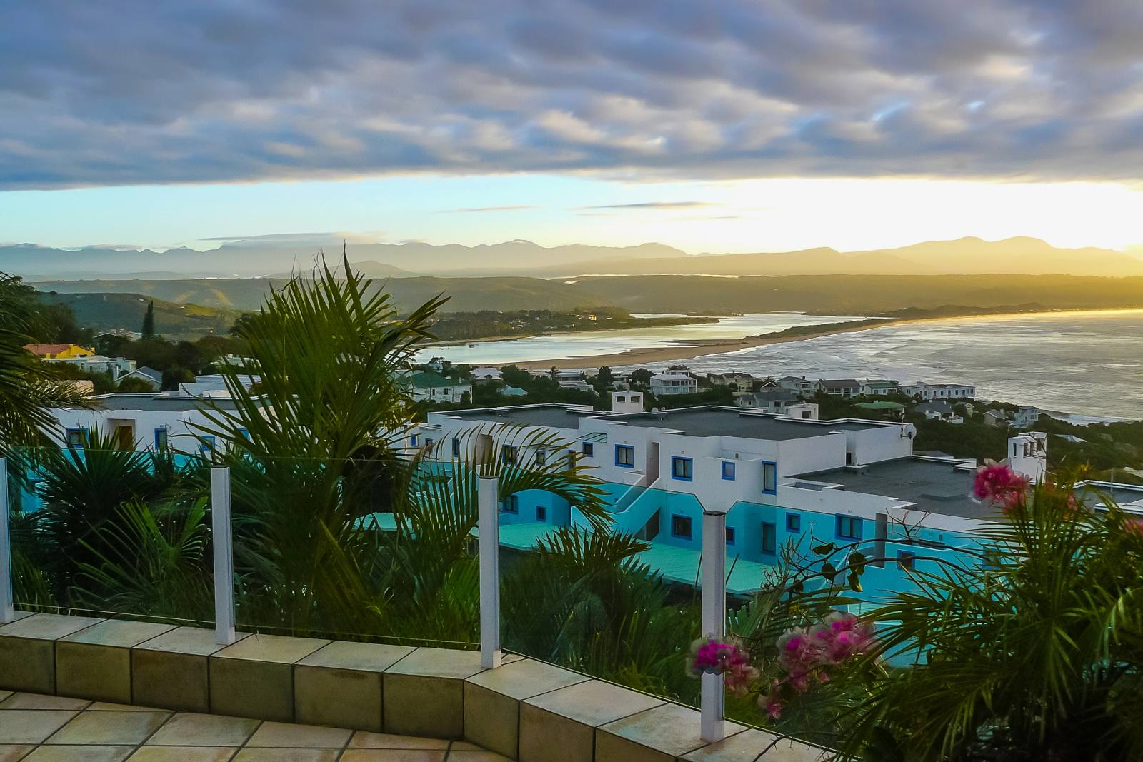 Blick über Hoteldächer und Palmen auf die Bucht von Mossel Bay am Abend